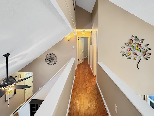 hall featuring baseboards, lofted ceiling, light wood-style floors, and an upstairs landing