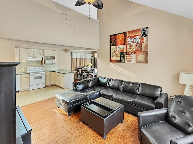 living room with light wood-type flooring, high vaulted ceiling, and a ceiling fan