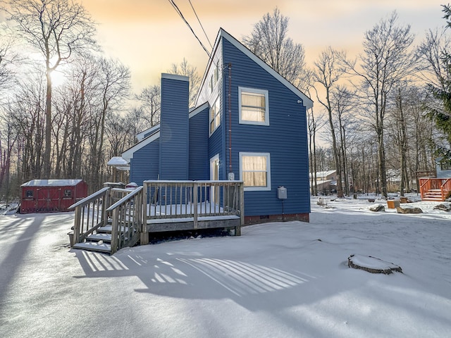 snow covered rear of property with a deck, an outdoor structure, a chimney, and crawl space