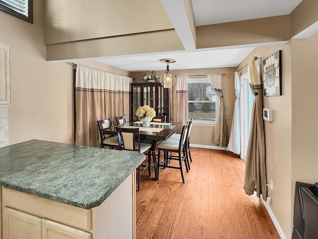 dining room with baseboards, beam ceiling, and light wood-style flooring