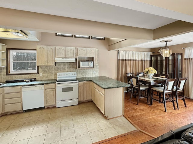 kitchen with under cabinet range hood, white appliances, tasteful backsplash, and dark countertops