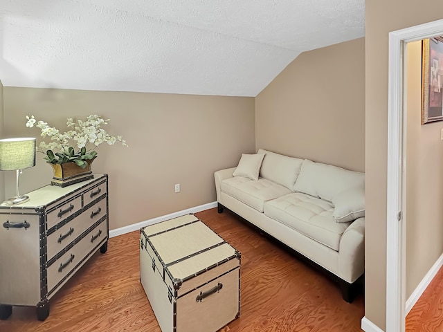 living area with vaulted ceiling, wood finished floors, baseboards, and a textured ceiling