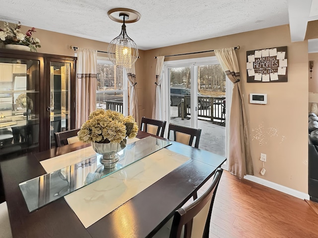 dining space with baseboards, a textured ceiling, an inviting chandelier, and wood finished floors