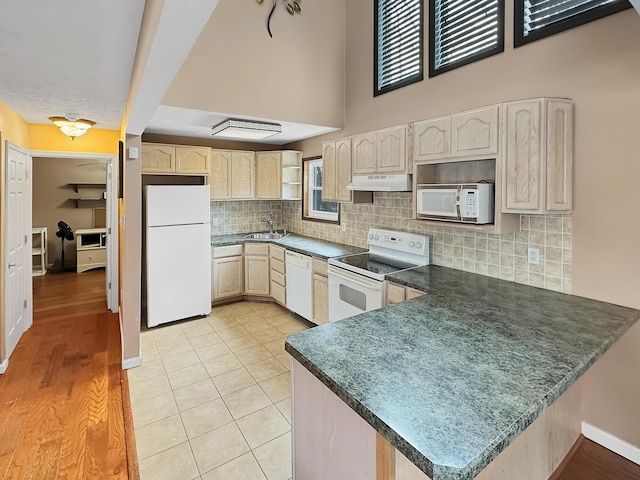 kitchen featuring under cabinet range hood, a sink, backsplash, white appliances, and a peninsula