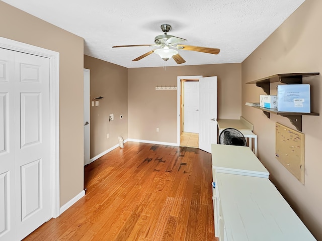 unfurnished office featuring light wood-style flooring, a textured ceiling, baseboards, and a ceiling fan