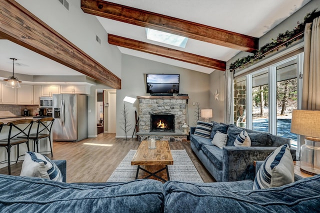 living area with visible vents, lofted ceiling with skylight, a stone fireplace, and light wood finished floors