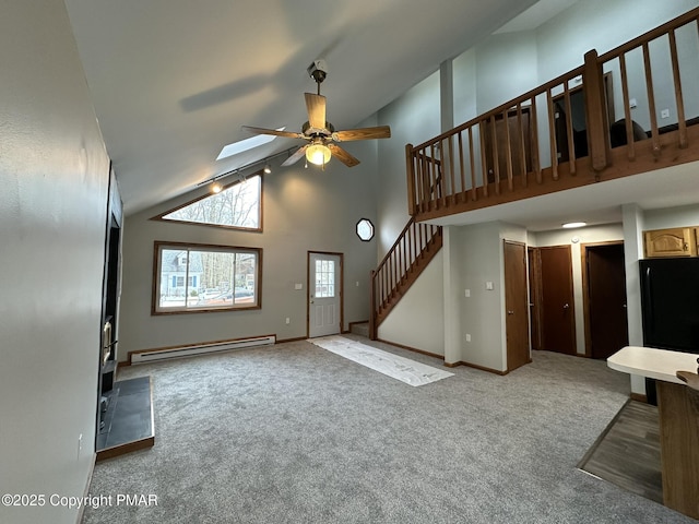 unfurnished living room with ceiling fan, a baseboard heating unit, a skylight, high vaulted ceiling, and carpet