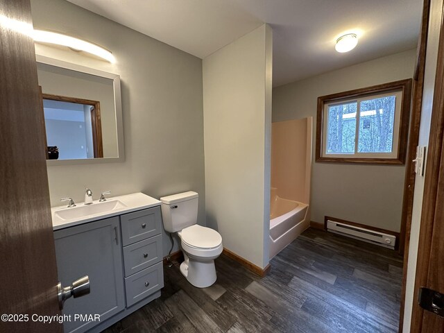 full bathroom with hardwood / wood-style flooring, washtub / shower combination, baseboard heating, vanity, and toilet