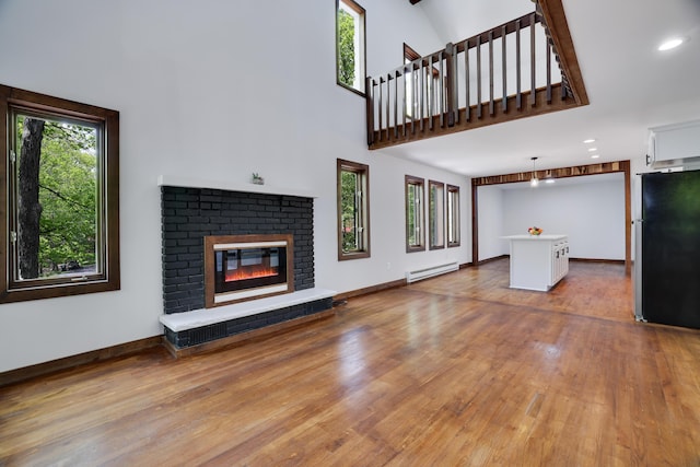 8210 Pine Grove Dr, East Stroudsburg, PA 18301 - unfurnished living room with baseboard heating, plenty of natural light, wood finished floors, a brick fireplace, and a towering ceiling