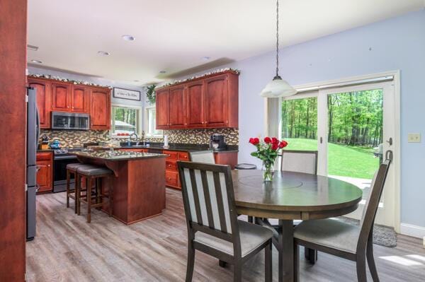 kitchen with stainless steel appliances, decorative backsplash, a center island, dark countertops, and light wood finished floors