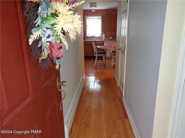 corridor featuring light wood-style floors, baseboards, baseboard heating, and a sink