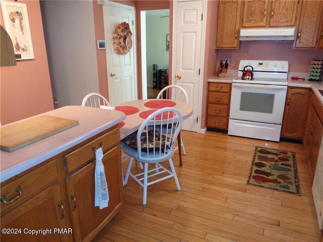 kitchen featuring white electric range oven, light countertops, light wood-style flooring, brown cabinetry, and under cabinet range hood