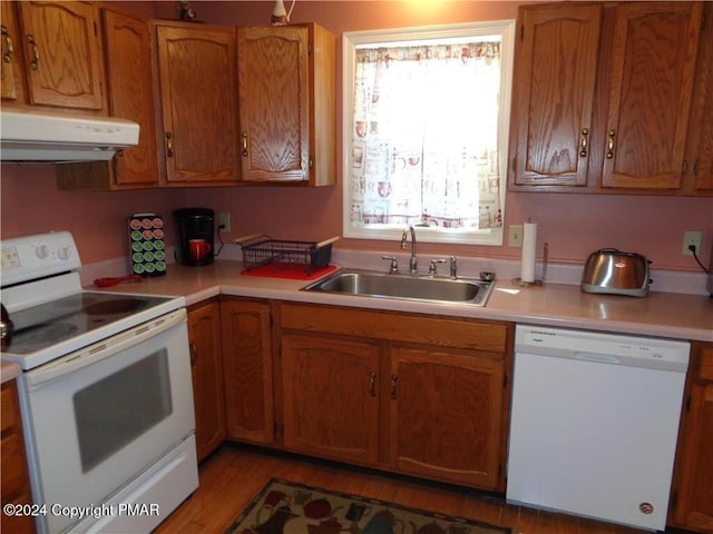 kitchen with range hood, brown cabinets, light countertops, a sink, and white appliances