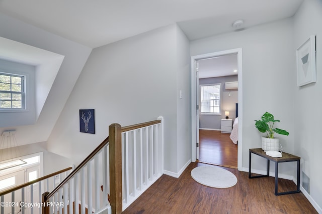 corridor with a wall unit AC, wood finished floors, an upstairs landing, and baseboards