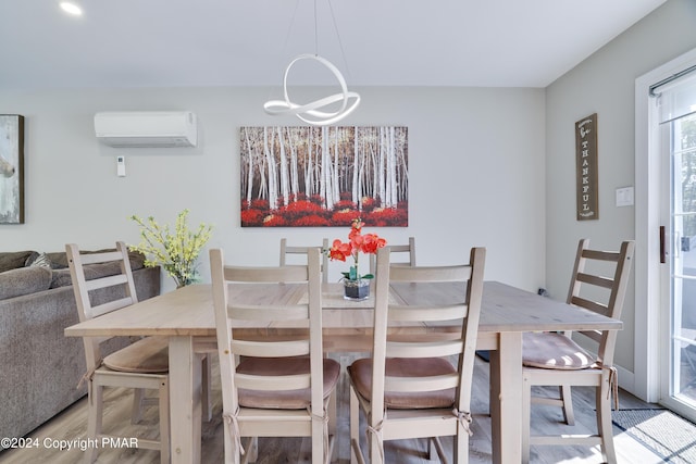 dining area with a chandelier, a wall unit AC, and light wood-style flooring