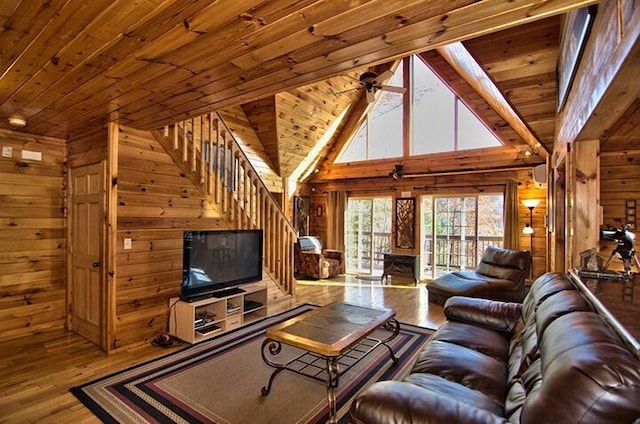 living room with wood ceiling, ceiling fan, stairway, wood finished floors, and wood walls