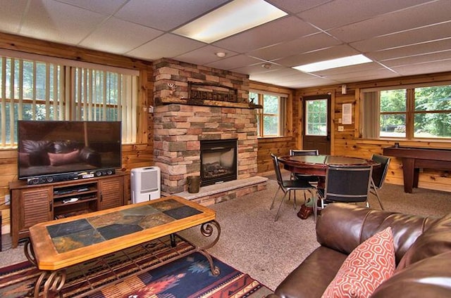 living area with a stone fireplace, wood walls, a drop ceiling, and carpet flooring