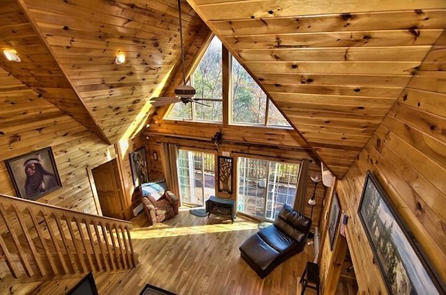 unfurnished living room with wood ceiling, wooden walls, high vaulted ceiling, and wood finished floors