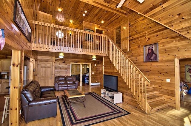 living room with stairway, a towering ceiling, wood ceiling, wood walls, and wood finished floors