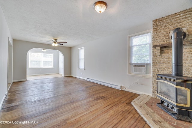 413 Old Rte 940, Pocono Pines, PA 18350 - unfurnished living room featuring a baseboard radiator, hardwood / wood-style floors, a wood stove, a ceiling fan, and plenty of natural light