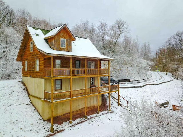 snow covered house featuring stairway and log siding