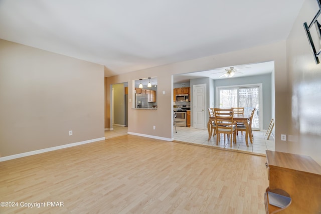 unfurnished living room with ceiling fan, light wood-style flooring, and baseboards