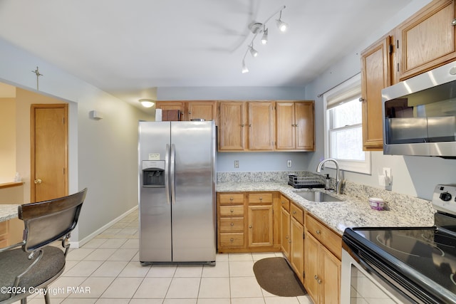 kitchen with appliances with stainless steel finishes, light tile patterned flooring, a sink, light stone countertops, and baseboards