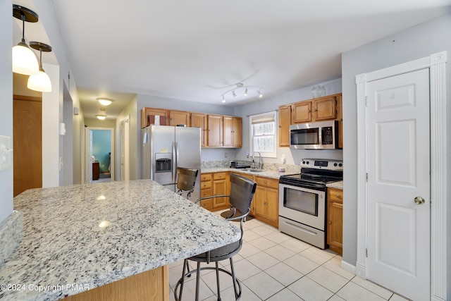 kitchen featuring light tile patterned floors, light stone counters, stainless steel appliances, a sink, and a kitchen breakfast bar