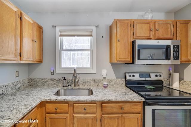 kitchen featuring appliances with stainless steel finishes, brown cabinetry, a sink, and light stone counters