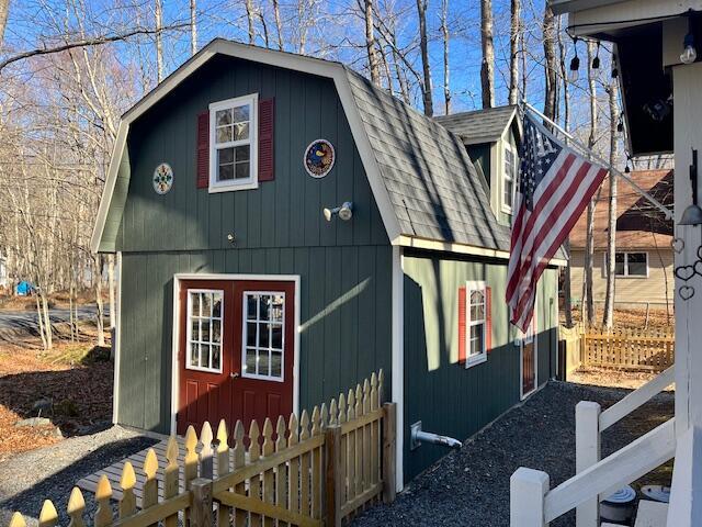 exterior space featuring a gambrel roof, a shingled roof, and an outdoor structure