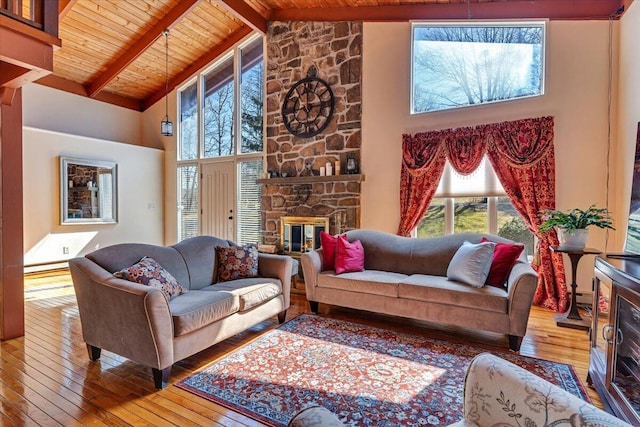 living area with high vaulted ceiling, wooden ceiling, hardwood / wood-style flooring, a stone fireplace, and beamed ceiling