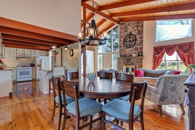 dining space featuring a stone fireplace, beamed ceiling, a notable chandelier, and light wood-type flooring