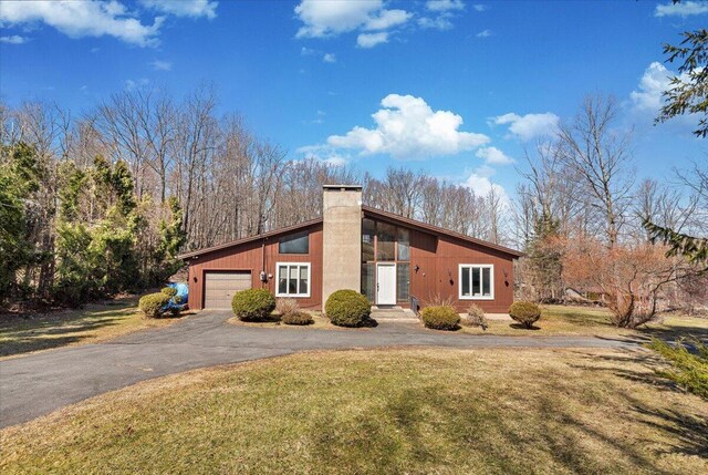 mid-century inspired home with a chimney, a front yard, a garage, and aphalt driveway