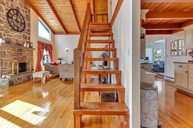 staircase with wood ceiling, lofted ceiling with beams, hardwood / wood-style flooring, and a fireplace