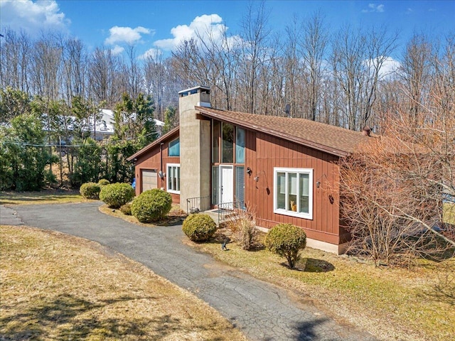 view of side of home with driveway, an attached garage, and a chimney