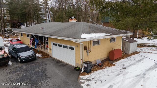 snow covered property with aphalt driveway, a chimney, and heating fuel