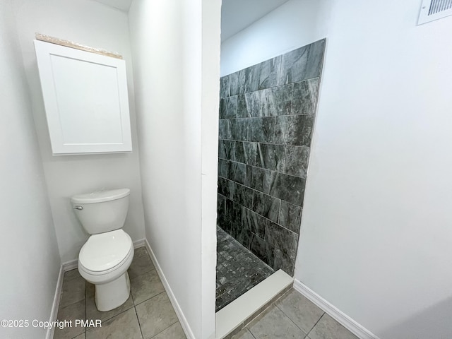 bathroom featuring tile patterned flooring, toilet, visible vents, baseboards, and a tile shower