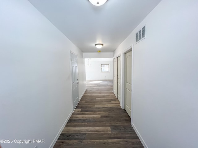 hallway with dark wood-style floors, visible vents, and baseboards