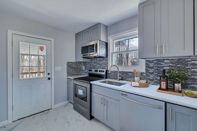 kitchen featuring a sink, gray cabinetry, marble finish floor, appliances with stainless steel finishes, and tasteful backsplash