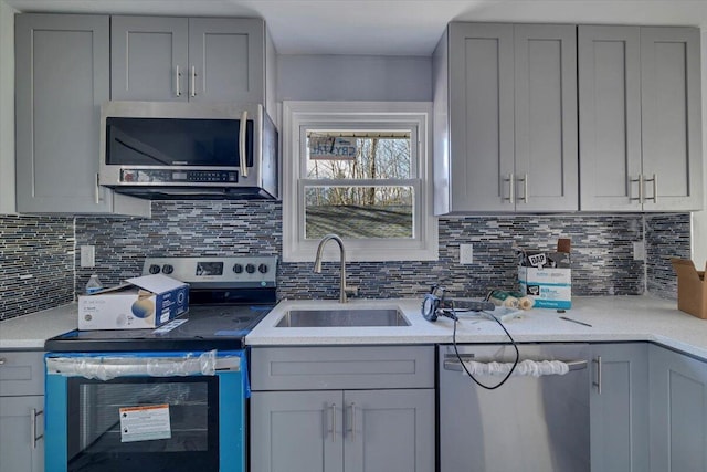 kitchen featuring a sink, backsplash, appliances with stainless steel finishes, and gray cabinetry