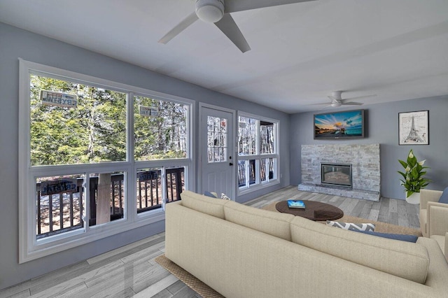 living room featuring plenty of natural light, a fireplace, a ceiling fan, and wood finished floors