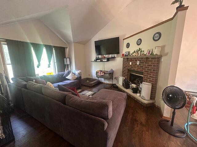 living area featuring wood finished floors, lofted ceiling, and a brick fireplace