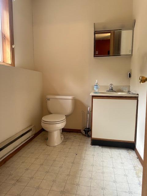 half bath with vanity, toilet, baseboards, and baseboard heating