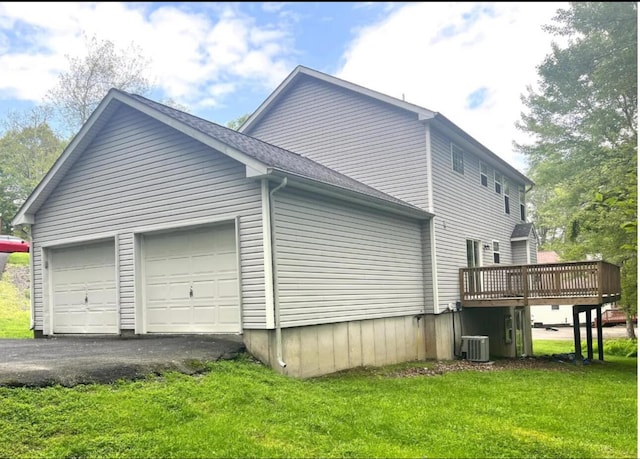 view of side of home with a lawn, cooling unit, an attached garage, a shingled roof, and a wooden deck