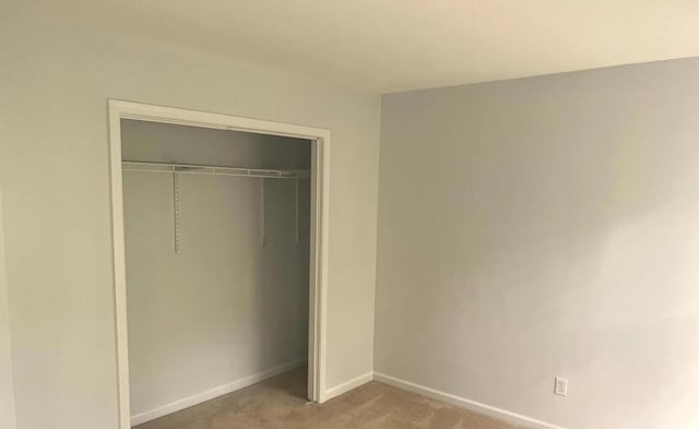 unfurnished bedroom with baseboards, a closet, and light carpet