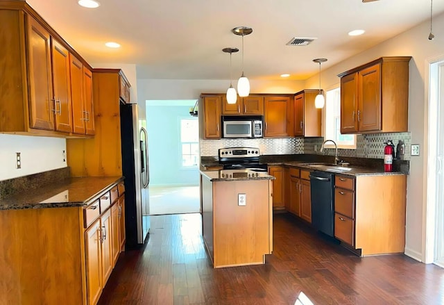 kitchen with a sink, a center island, appliances with stainless steel finishes, brown cabinetry, and dark wood-style flooring