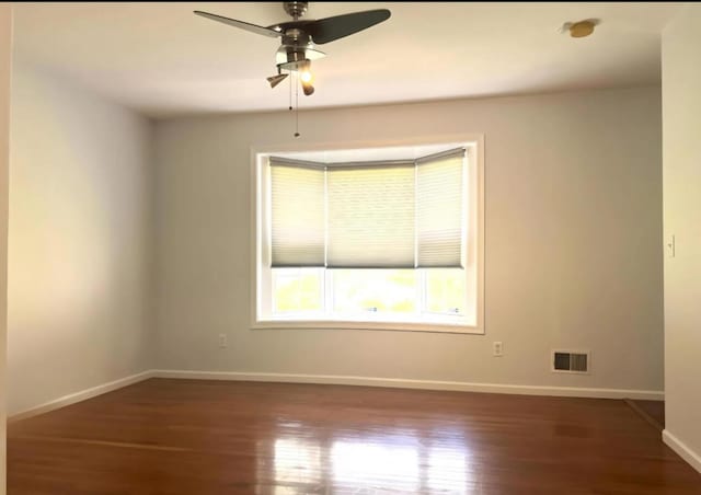 unfurnished room featuring visible vents, baseboards, dark wood-style floors, and a ceiling fan