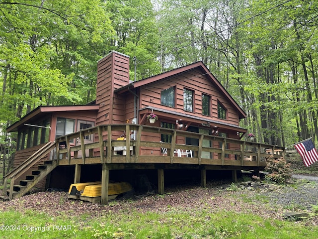 back of property with a forest view, a chimney, stairway, and a deck