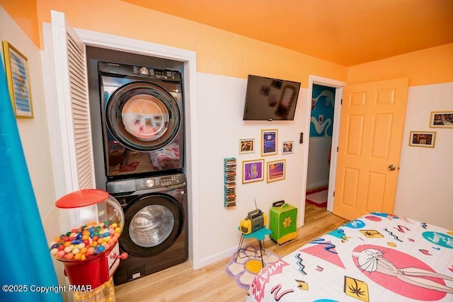 bedroom with stacked washer / drying machine, baseboards, and wood finished floors