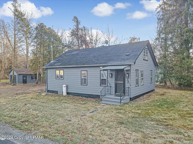 view of front of property with a shingled roof, an outbuilding, and a front lawn